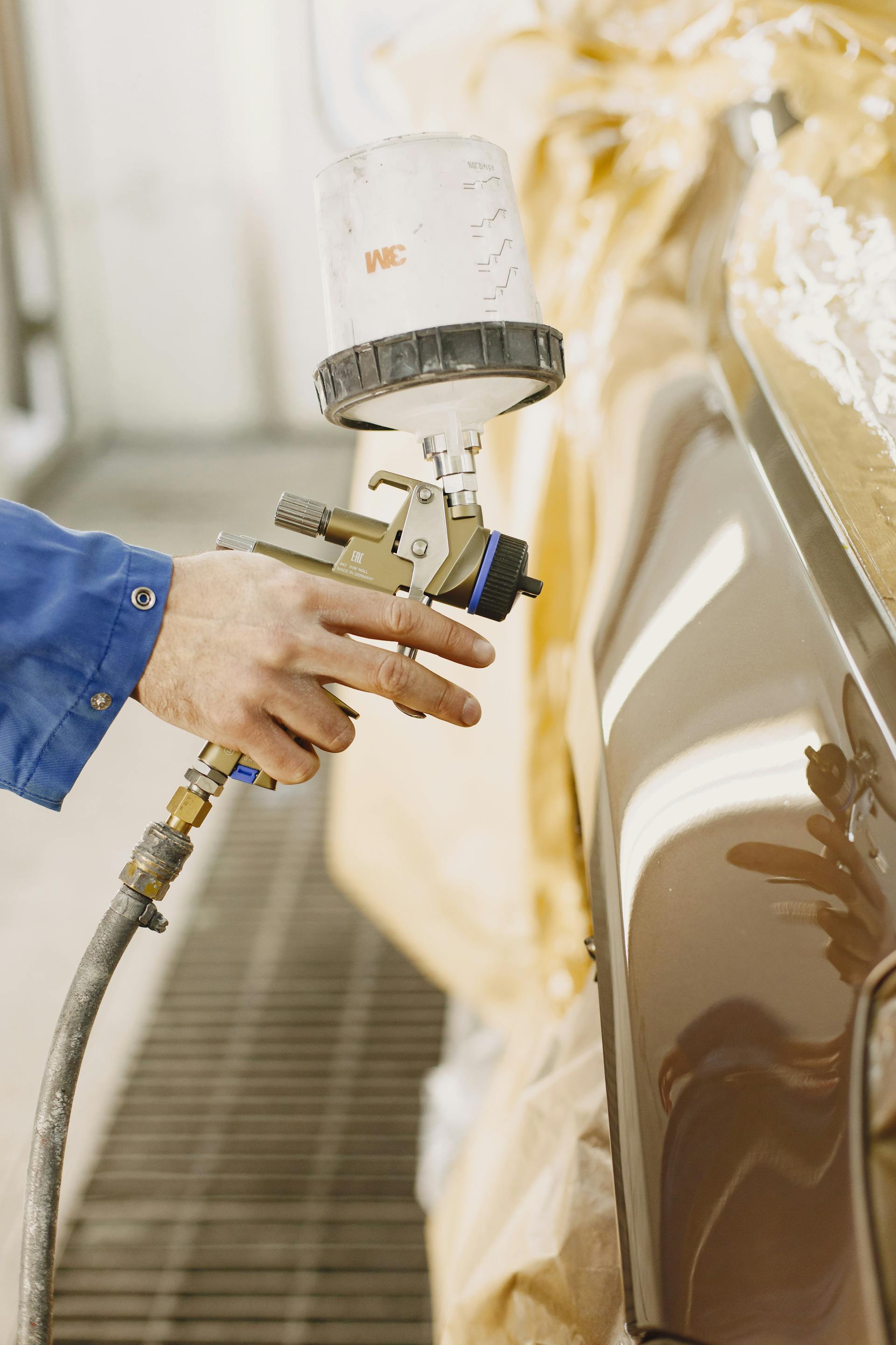 Technician applying a fresh coat of paint to a car panel with a spray gun