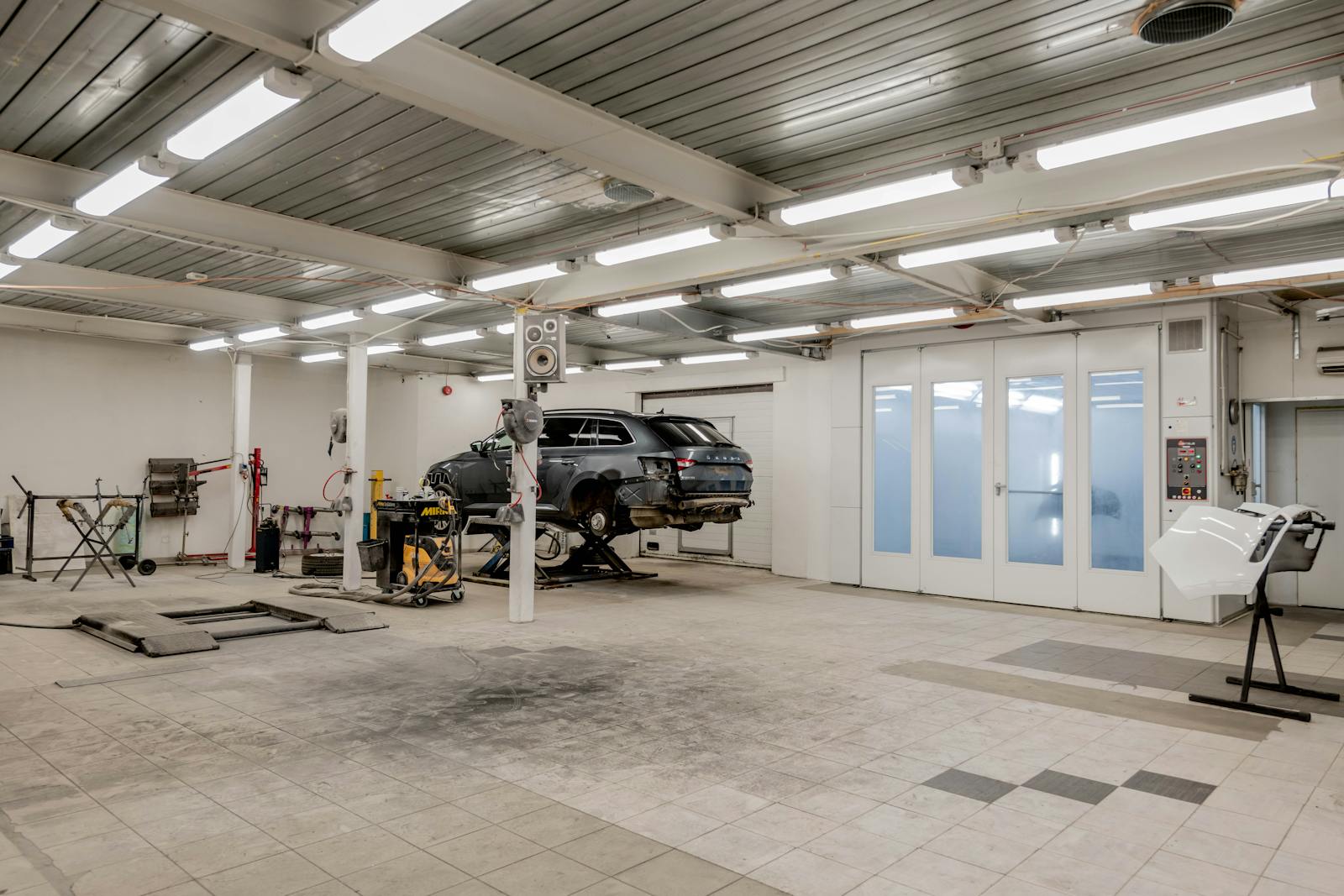 Spacious, well-lit auto body shop interior with a vehicle on a lift